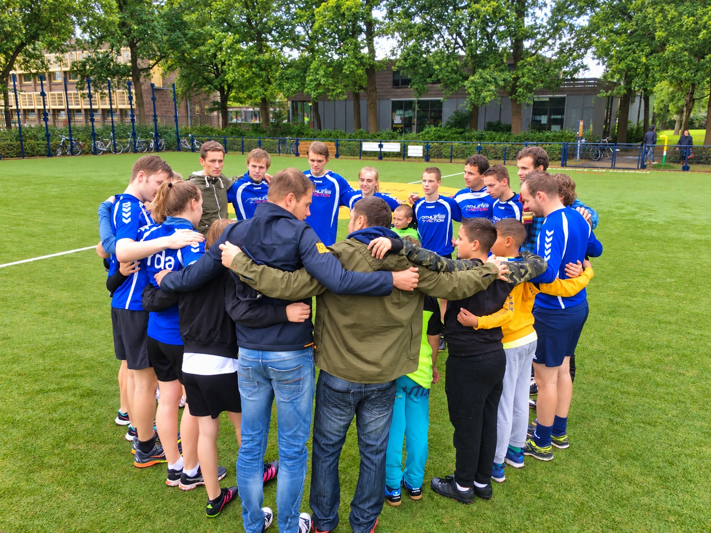 Athletes and young players with their arms around one another in a team huddle on a football pitch